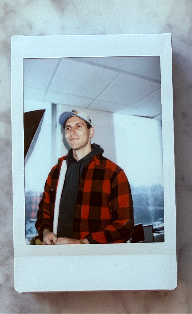Polaroid photo of Gabe wearing a red plaid shirt and cap on a marble surface